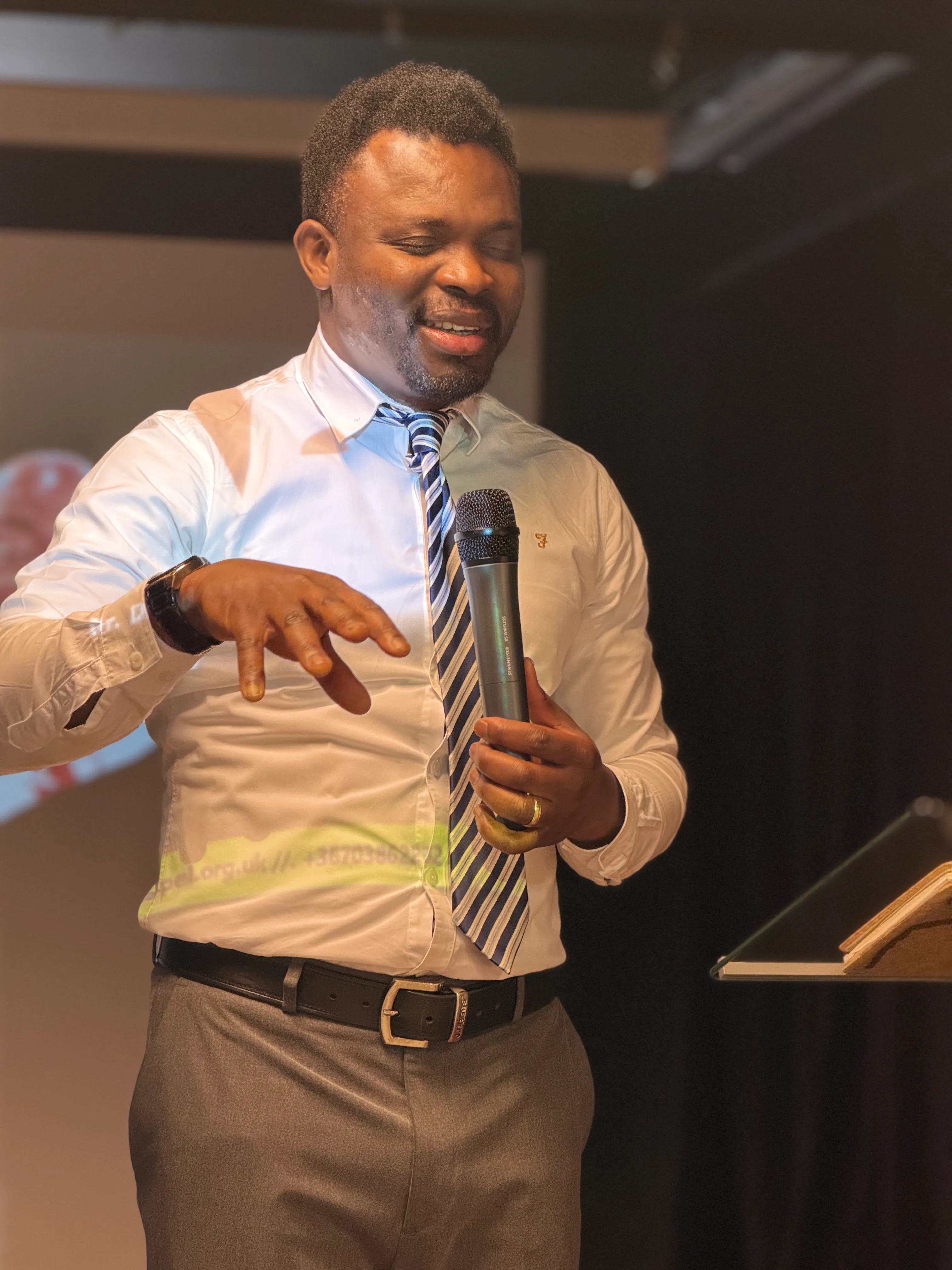 Pastor James Samuel preaching, a microphone in his hand