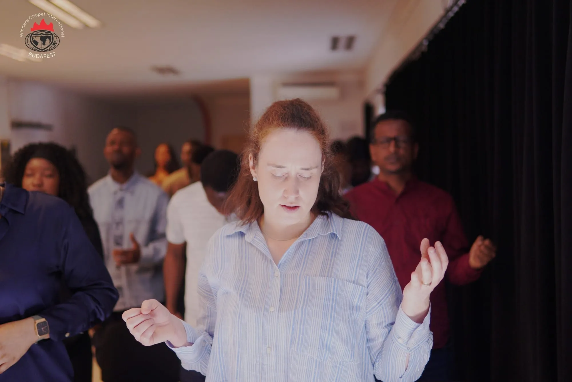 A woman praying with open hands among a room of people in prayer