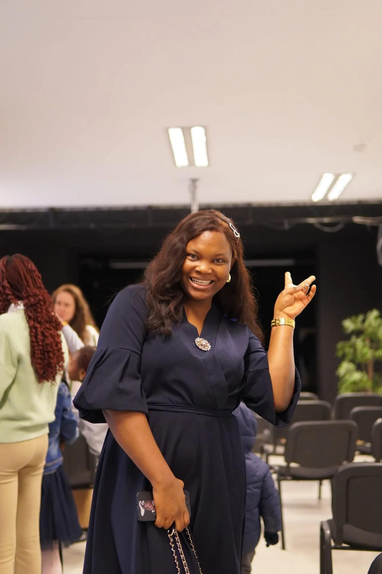 A woman in a dark dress smiling and gesturing as she walks in
